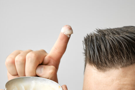 Man applying a clay, pomade, wax, gel or mousse from round metal box for styling his hair after barbershop hair cut. Advertising concept of mans products. Treatment and care against lost of hair